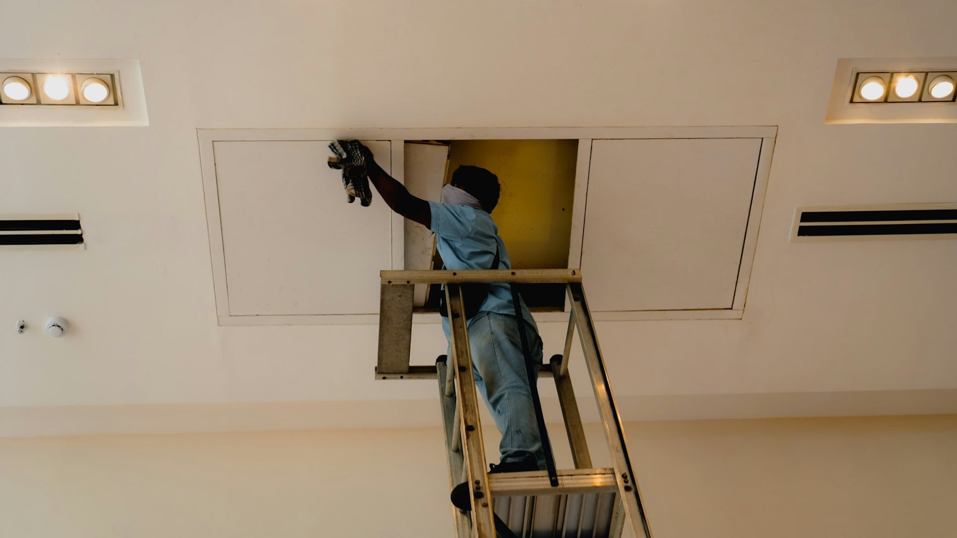 Technician removing a ceiling air vent cover for cleaning